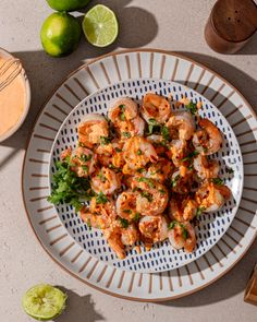 a white plate topped with shrimp and garnish next to limes on a table