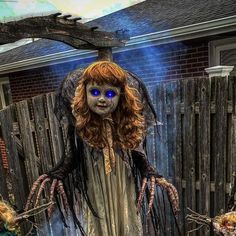 a woman dressed as a scary doll with blue eyes and long hair standing in front of a fence