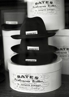 black and white photograph of hats stacked on top of each other in containers with labels