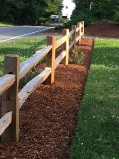 a wooden bench sitting on the side of a road next to a lush green field