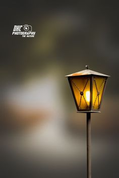 an old fashioned street lamp with a yellow light shining on it's side and dark background