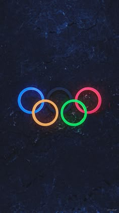 the olympic rings are lit up in different colors and sizes on a black surface with dark background