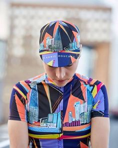 a woman wearing a colorful shirt and cycling cap looking down at her cell phone while standing in the street