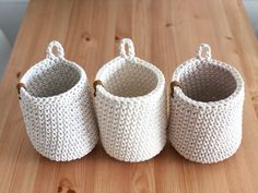 three white knitted baskets sitting on top of a wooden table next to each other