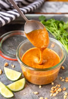 a spoon full of sauce being lifted from a glass bowl with limes and cilantro on the side