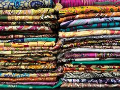 many different colored fabrics are stacked on top of each other in this photo, there is a large stack of colorful cloths