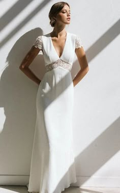 a woman standing in front of a white wall wearing a dress with lace on it