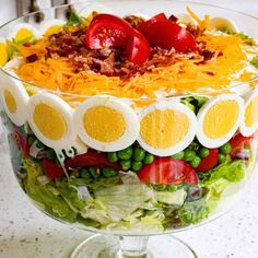 a salad with hard boiled eggs, tomatoes, peas and cheese on top in a glass dish