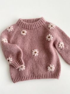 a pink sweater with white flowers on the front and back, sitting on a white surface