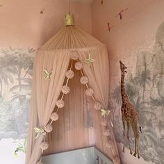 a giraffe standing next to a bed in a room with pink walls and curtains