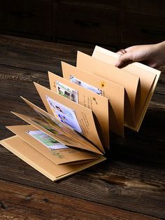 a person is holding several folders on top of a wooden table with their hands