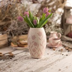 pink tulips in a white vase on a table next to teacups