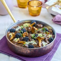 a bowl filled with meat and blackberries on top of a purple place mat next to glasses