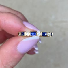 a woman's hand holding a yellow gold ring with blue sapphires and diamonds