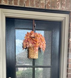 a basket filled with flowers hanging from the side of a front door, in front of a window