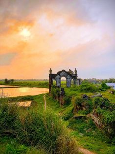 an old building sitting on top of a lush green field next to a lake at sunset