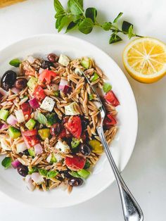 a white bowl filled with pasta salad next to an orange slice and fork on a table