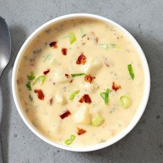 a white bowl filled with soup on top of a gray table next to a spoon