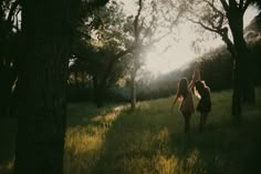 two girls are walking through the woods with their arms in the air as the sun shines behind them