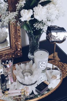 a table topped with a vase filled with white flowers and lots of other items next to a mirror