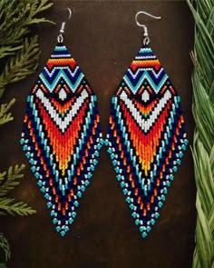 a pair of colorful beaded earrings sitting on top of a wooden table next to plants