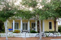 two bikes are parked in front of a yellow house with white picket fence and trees