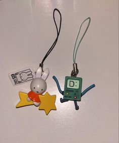 two keychains that are shaped like cartoon characters on a white table with a black cord