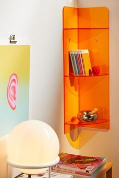 an orange shelf is next to a white chair and bookshelf with magazines on it