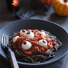 a black plate topped with spaghetti covered in googly eyes and ghost's eyeballs