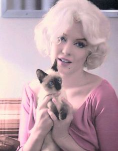 a woman holding a cat in her hands while sitting on a couch next to a window