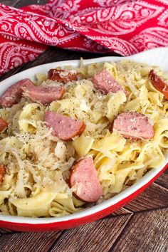 a white bowl filled with pasta and ham on top of a wooden table next to a red bandanna