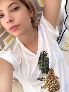 a woman laying on top of a bed next to a white pillow with a pineapple on it