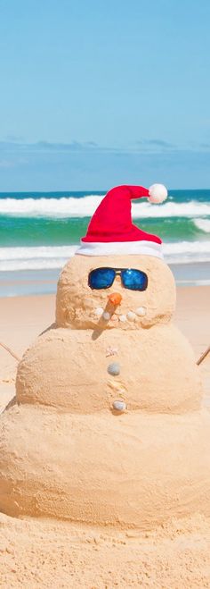 a snowman wearing sunglasses and a santa hat on the beach