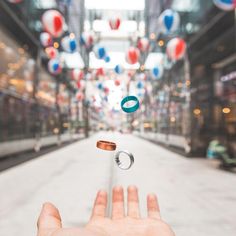 a hand is throwing rings in the middle of an empty street with balloons floating above