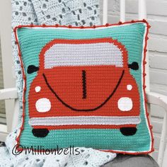 a crocheted pillow with a red car on it sitting on a white chair