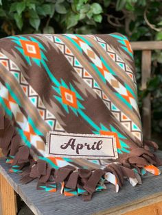 a brown and turquoise blanket sitting on top of a wooden table next to a bush