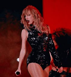 a woman in a black bodysuit on stage with her legs spread out and mouth open