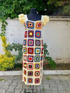 a crocheted dress on display in front of a white wall and green plants