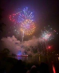 fireworks are lit up in the night sky above water and clouds as people look on