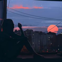 a person sitting on a window sill looking out at the city and setting sun