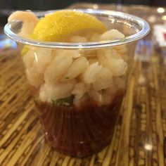 a plastic cup filled with food on top of a wooden table next to a lemon