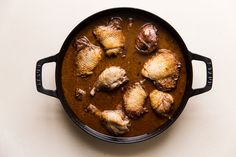 a pan filled with meat and sauce on top of a white table next to a spoon