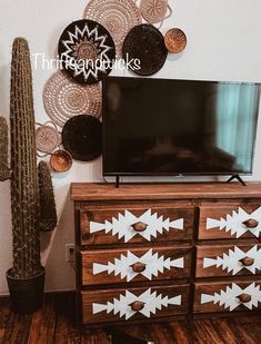 a flat screen tv sitting on top of a wooden dresser next to a cacti