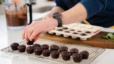 a person reaching for some chocolates on a cooling rack with other pastries in the background