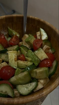 a wooden bowl filled with cucumbers, tomatoes and other vegtables