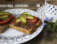 two pieces of bread with tomatoes, avocado and tomato slices on them next to a cup of coffee