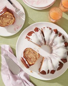 a bundt cake with white icing on a plate next to two glasses of orange juice