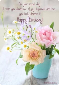 a vase filled with flowers sitting on top of a wooden table next to a happy birthday card