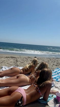 three women in bikinis are laying on the beach