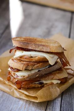 a grilled cheese sandwich is stacked on top of brown paper and sits on a wooden table